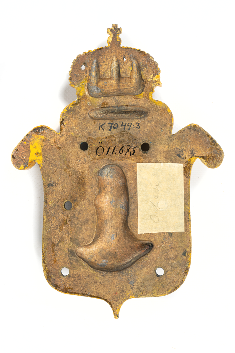 Stävsköld av brons, 21 cm hög, gulmålad Oden-bild mot blå botten.
Utgöres av sköld med krona, inom skölden på mörkblå botten guden Odens bild. Gudabilden och kanterna på skölden målade i gult, kronan i gult, rött och vitt.