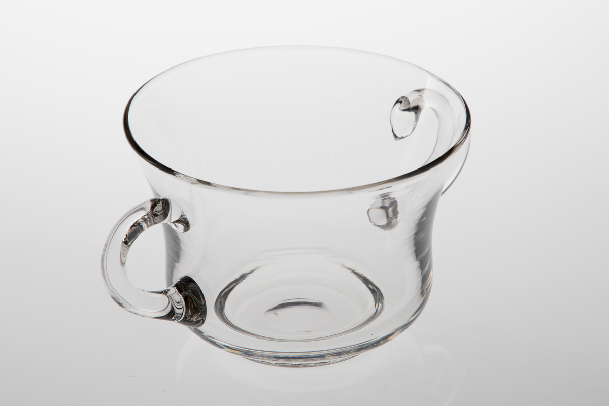 Sukkerkopp i klart glass. Konkav korpusform på lav fotring. To diametralt påsatte hanker.