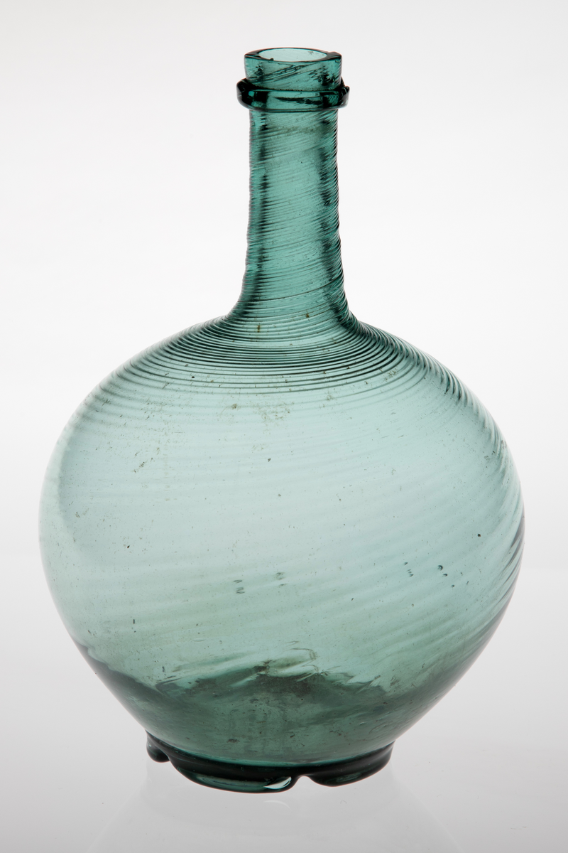 Kuleformet karaffel med lang hals. Glasset er lysegrønt, korpus og hals er dekket med tette, sterkt dreide rifler. Overgangen mellom hals og munning er markert med en smal ring. Korpus hviler på en tunget fotring med puntemerke.