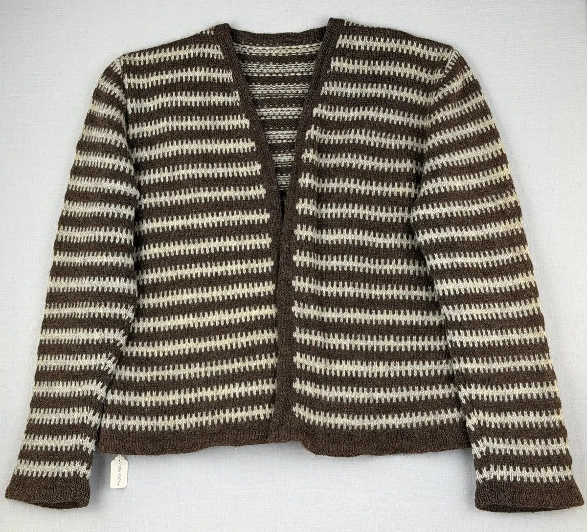 En v-ringad kofta, stickad i mönstrad slätstickning, av 3-trådigt ullgarn. Nederkanterna har en fåll, med ett avigt varv i vikningen, som är fastsydd med kaststygn.