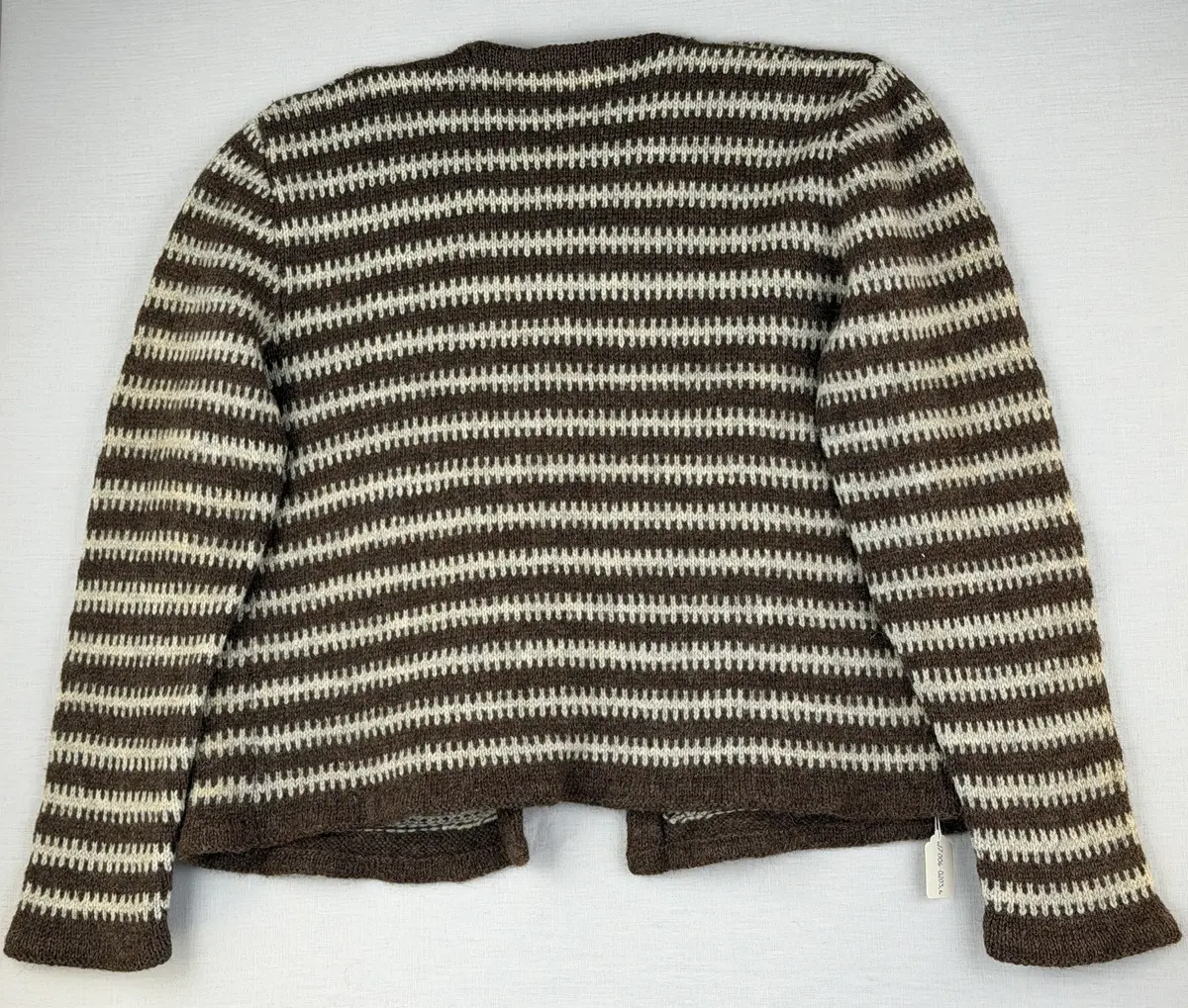 En v-ringad kofta, stickad i mönstrad slätstickning, av 3-trådigt ullgarn. Nederkanterna har en fåll, med ett avigt varv i vikningen, som är fastsydd med kaststygn.