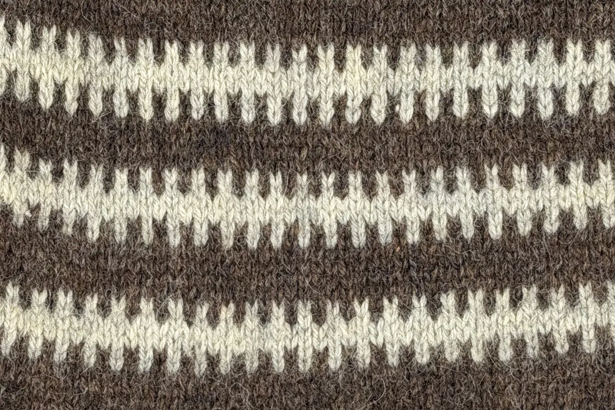 En v-ringad kofta, stickad i mönstrad slätstickning, av 3-trådigt ullgarn. Nederkanterna har en fåll, med ett avigt varv i vikningen, som är fastsydd med kaststygn.