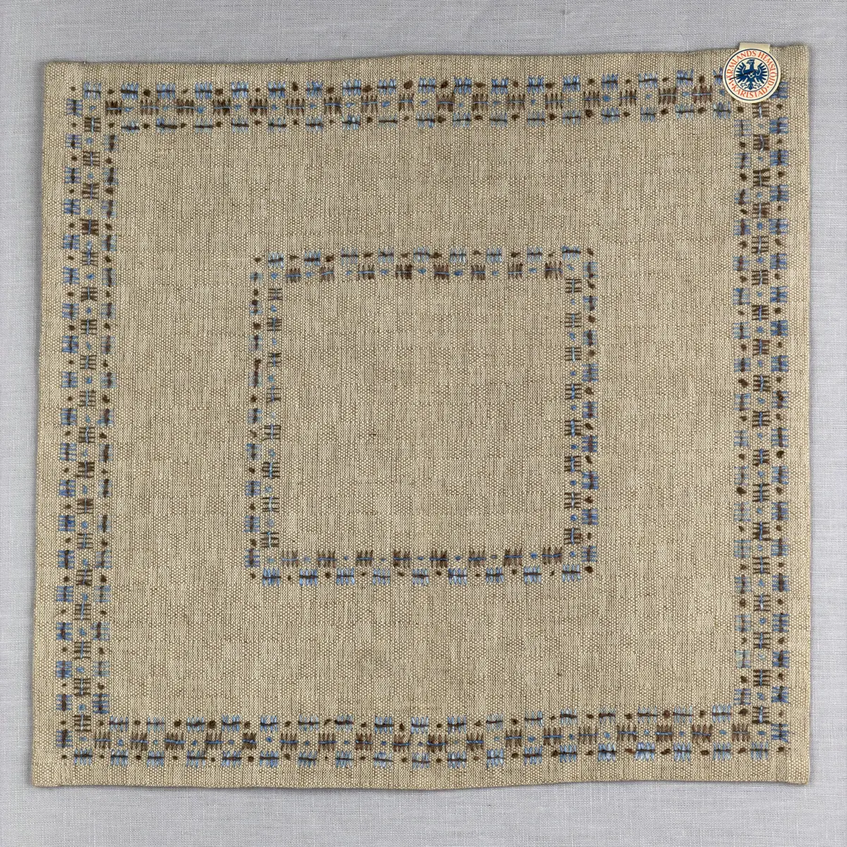 Bordsduk gjord av handvävt linnetyg i sålldräll och broderi utfört med lintråd i rätvinkligt lagda förstygn översydda med läggsöm samt knutar. 
Duken har raka hörn och 12mm breda dubbelvikta fållar runt om, som är fastsydda med smygstygn. 