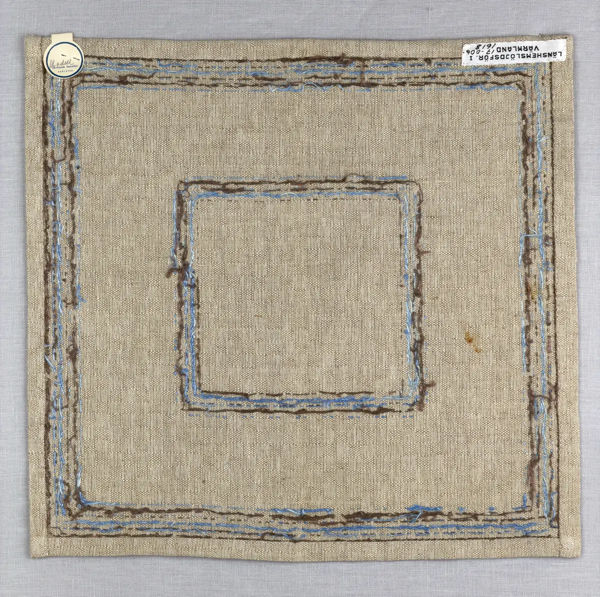 Bordsduk gjord av handvävt linnetyg i sålldräll och broderi utfört med lintråd i rätvinkligt lagda förstygn översydda med läggsöm samt knutar. 
Duken har raka hörn och 12mm breda dubbelvikta fållar runt om, som är fastsydda med smygstygn. 