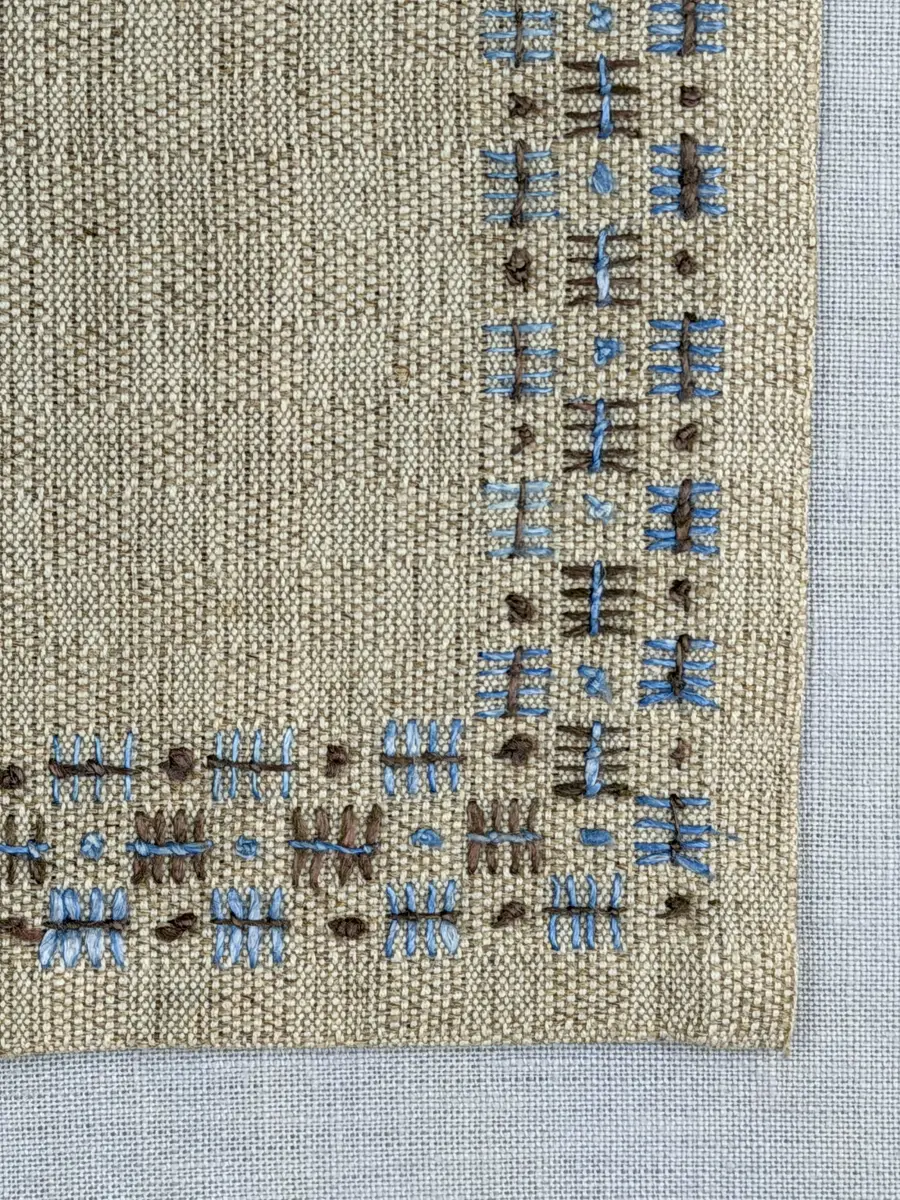 Bordsduk gjord av handvävt linnetyg i sålldräll och broderi utfört med lintråd i rätvinkligt lagda förstygn översydda med läggsöm samt knutar. 
Duken har raka hörn och 12mm breda dubbelvikta fållar runt om, som är fastsydda med smygstygn. 