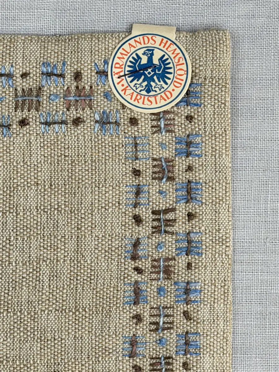 Bordsduk gjord av handvävt linnetyg i sålldräll och broderi utfört med lintråd i rätvinkligt lagda förstygn översydda med läggsöm samt knutar. 
Duken har raka hörn och 12mm breda dubbelvikta fållar runt om, som är fastsydda med smygstygn. 