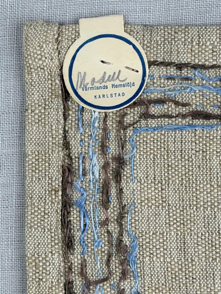 Bordsduk gjord av handvävt linnetyg i sålldräll och broderi utfört med lintråd i rätvinkligt lagda förstygn översydda med läggsöm samt knutar. 
Duken har raka hörn och 12mm breda dubbelvikta fållar runt om, som är fastsydda med smygstygn. 