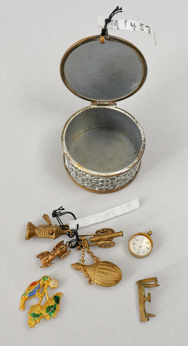 Nipperask innehållande diverse berlocker. Cylindrisk form med gångjärnförsett lock. Ornerat.