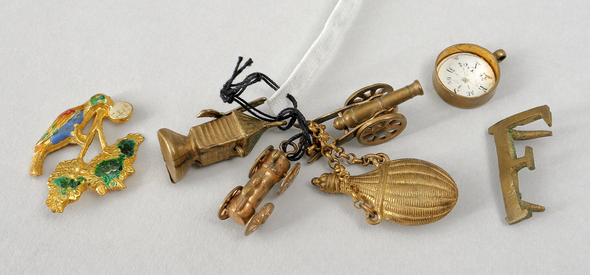 Nipperask innehållande diverse berlocker. Cylindrisk form med gångjärnförsett lock. Ornerat.