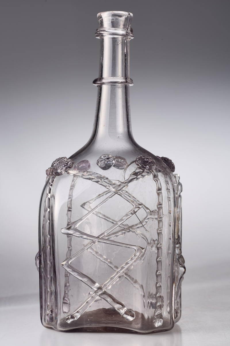 Åttekantet butelje med zirater og bringebær. Annenhver bringebær er svakt manganfarget. Pontmerke under flaska. To påsmeltede ringer på halsen.