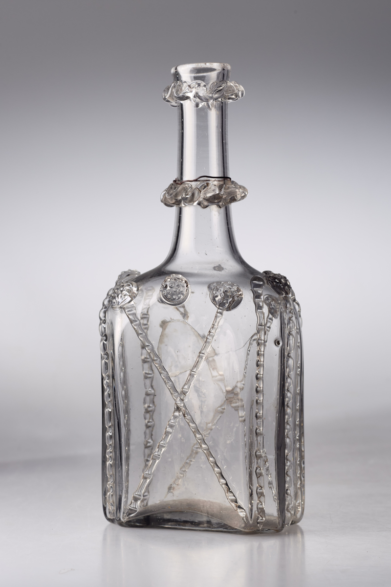 Åttekantet butelje med zirater og bringebær. Pontmerke under flaska. To påsmeltede ringer på halsen.