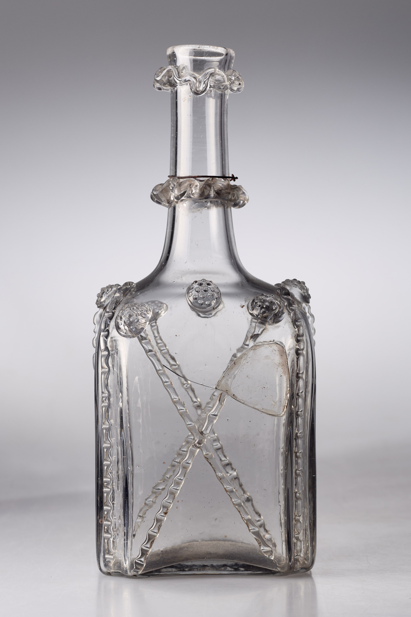 Åttekantet butelje med zirater og bringebær. Pontmerke under flaska. To påsmeltede ringer på halsen.