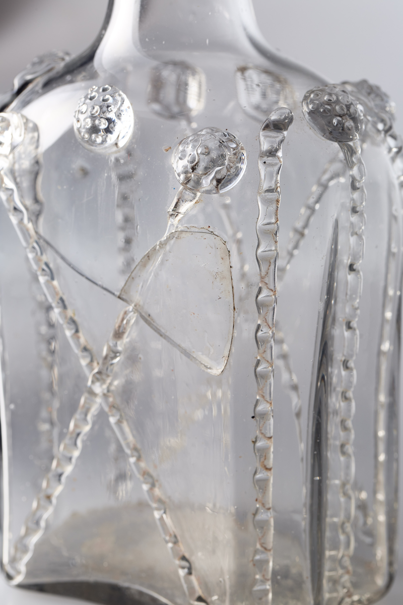 Åttekantet butelje med zirater og bringebær. Pontmerke under flaska. To påsmeltede ringer på halsen.