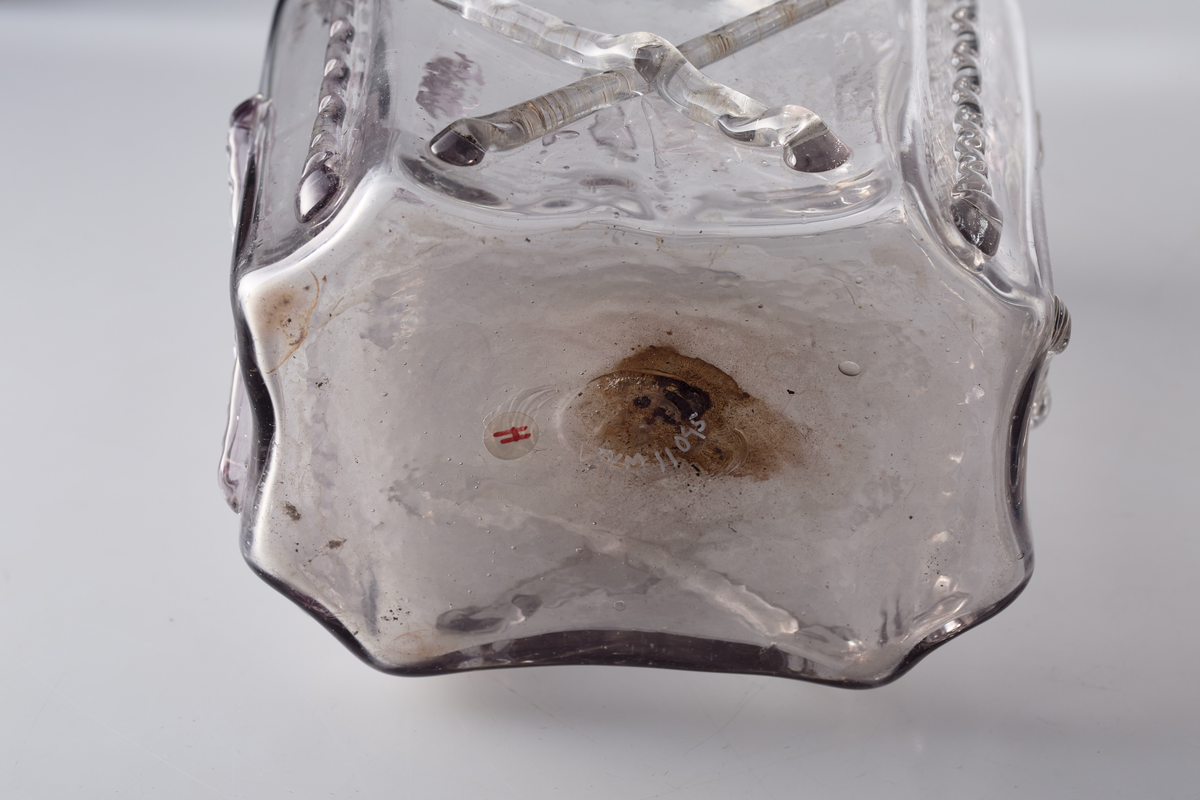 Åttekantet butelje med zirater og bringebær. Annenhver bringebær er svakt manganfarget. Pontmerke under flaska. To påsmeltede ringer på halsen.