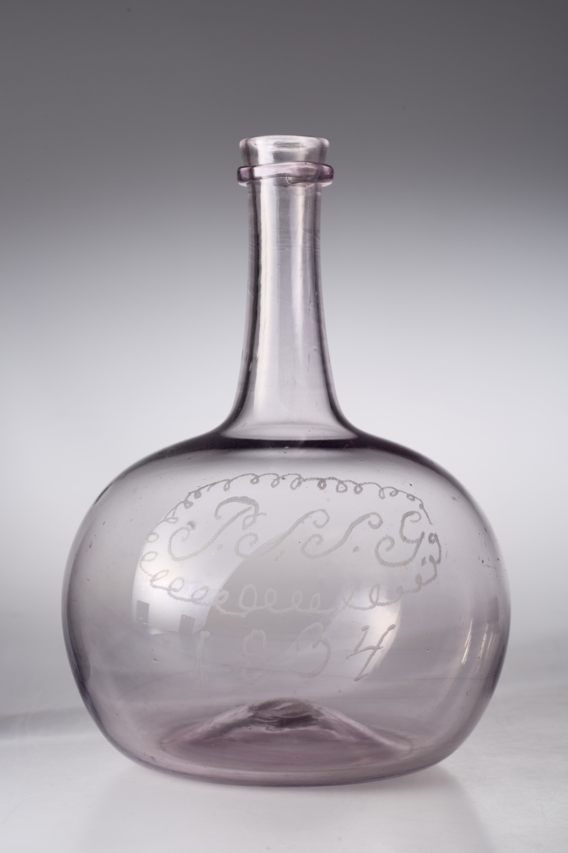 Karaffel med påsmeltet ring rundt kragen og pontmerke. Enkel gravering. Glasset er ikke helt klart, men har en anelse mangan.