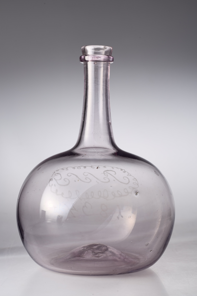 Karaffel med påsmeltet ring rundt kragen og pontmerke. Enkel gravering. Glasset er ikke helt klart, men har en anelse mangan.