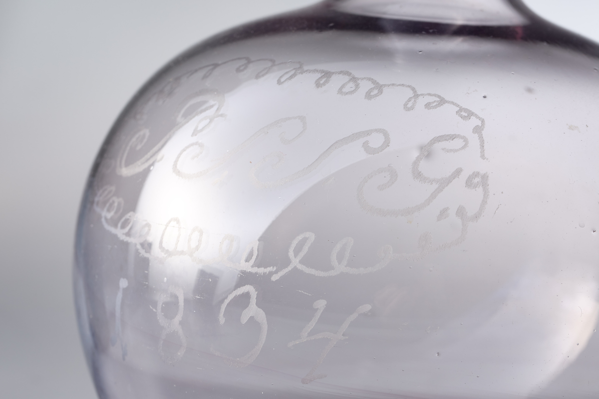 Karaffel med påsmeltet ring rundt kragen og pontmerke. Enkel gravering. Glasset er ikke helt klart, men har en anelse mangan.