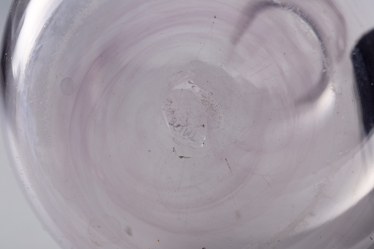 Karaffel med påsmeltet ring rundt kragen og pontmerke. Enkel gravering. Glasset er ikke helt klart, men har en anelse mangan.