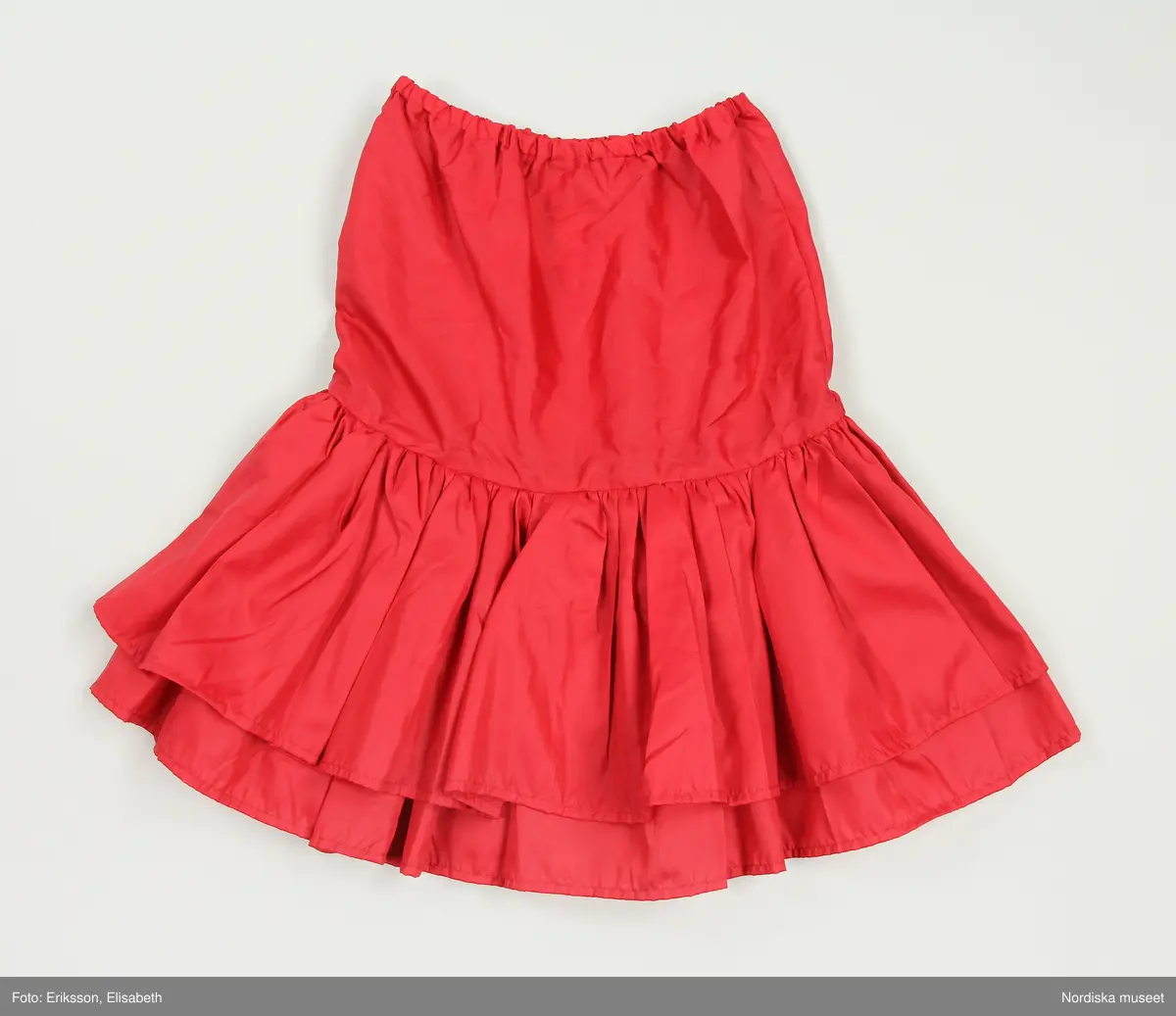 Grön mockakavaj och kjol. 
a) Dubbelknäppt kavaj som knäpps med metallknappar och passpoalerade knapphål. Knapparna är hela vägen upp (8 st på var sida) men två knappar döljs av slaget. Ett knapphål i midjehöjd och ett på slaget  på vänter sida, även de passpolerat och en grön plastknapp på insida att knäppa den med. Alla metallknapparna fastsydda med små "plastknappar" som förstärkning under, vid fickan är knapparna enbart fastsydda genom en lager av fickpåsarna.  
Axelklaffar som hålls på plats av metallknappar.
Söm mitt på ärmen med en stickning och en söm under ärmen.
Lodrätta infällda fickor med stolpe på framstycket 
Knytslelfar bak, fastsydda i längsgånde sömmar på bakstycket. 
På insidan av framstycket är det en maskinvävdetikett fastsydd. Texten säger 38 Tonnie 9-10 och runt detta står det skrivet i en cirkel MADE IN SWEDEN PRODUCED BY TONNIE DESIGN AB - STOCKHOLM -  SWEDEN - LW. Under cirkeln står det Von opp/xs

b) Kjol med besparing till stussen och utställda paneler 
På besparingen fram är det lodrätta passpolerade fickor med en knapp, rött foder i fickpåsarna. 
4 cm bred linning med dragkedja och knapp bak. 
På insidan stämplade nummer med vitt, samma nummer på alla delar. 

c) Underkjol, lös röd underkjol med två volanger sydda tillsammans på en besparing, den övre volangen lite kortare än den undre. Resår i midjan, trätt i en dragsko. 
På insidan av underkjolen är det en maskinvävdetikett fastsydd. Texten säger 38 Tonnie 9-10 och runt detta står det skrivet i en cirkel MADE IN SWEDEN PRODUCED BY TONNIE DESIGN AB - STOCKHOLM -  SWEDEN - LW. Under cirkeln står det Von opp/xs

/ Magdalena Fick 2025/07/10