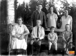 Kalla Persson sitter i korgstolen,
Bakom bänken står Agda oc