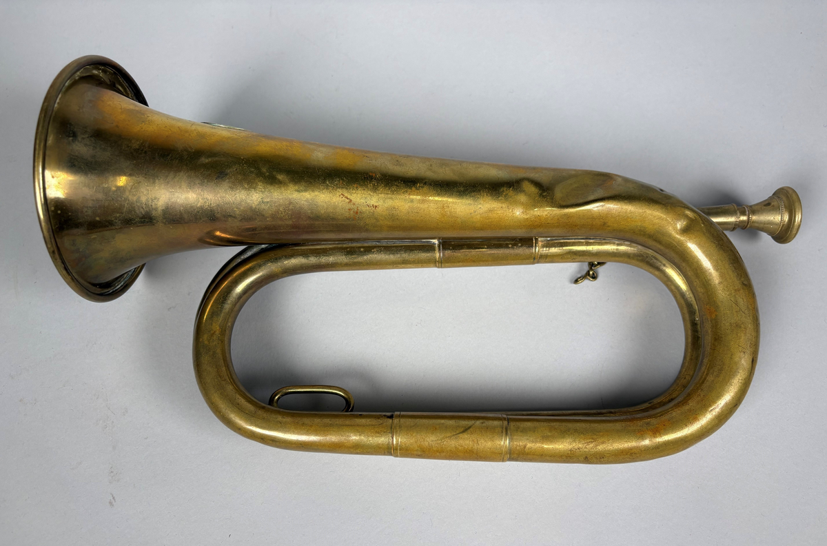 Posthorn, trompettype av messing. 
På hornet er anbrakt et rundt skilt med postemblem. Hornet har noe bulker.