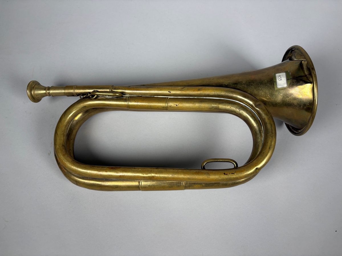 Posthorn, trompettype av messing. 
På hornet er anbrakt et rundt skilt med postemblem. Hornet har noe bulker.