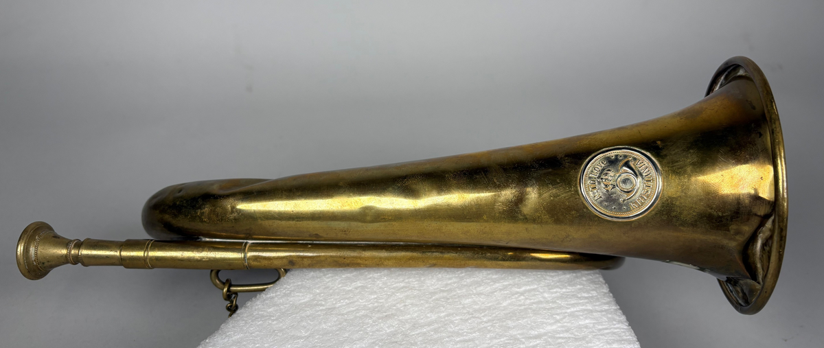 Posthorn, trompettype av messing. 
På hornet er anbrakt et rundt skilt med postemblem. Hornet har noe bulker.