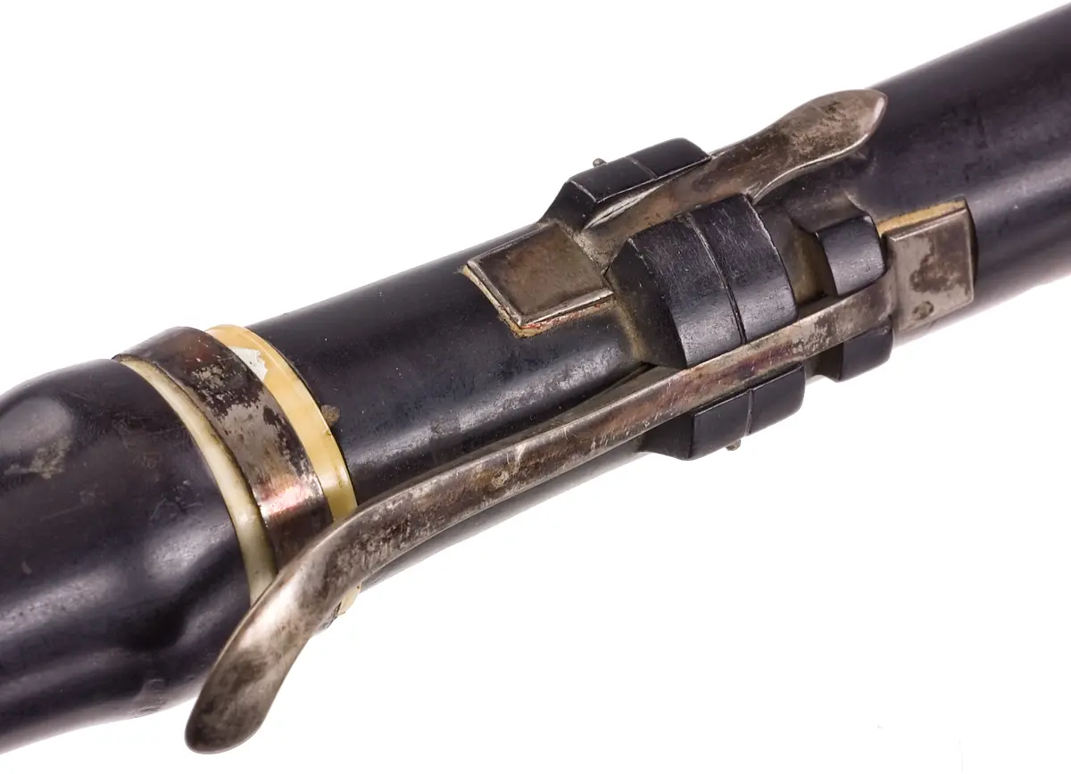 Tvärflöjt i mörkt trä med ringar av elfenben. 5 delar. Sprickor i munstycke, päron, undre mellandelen och ringen mellan mellanstyckena. Den senare är lagad med en metallring satt runt originalringen. Konisk form. 7 klaffar med kvadratisk platta och bocklagring.