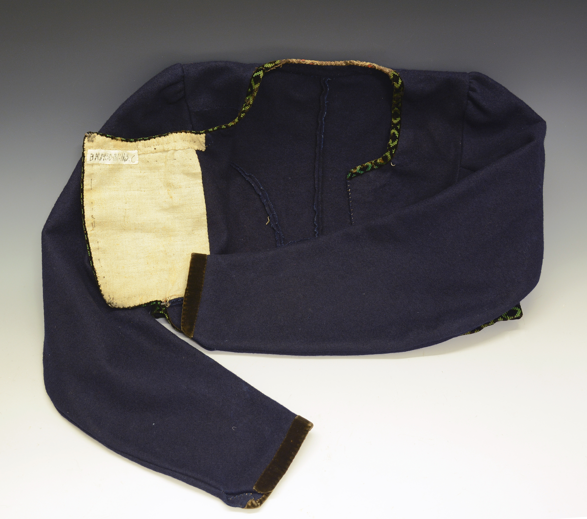 Drakt som består av A) overdel, B) stakk, C) trøye og D) forkle. Opplysninger fra protokollen: c) Trøye av blaatt vadmaal kanta med grøne og svartmynstra fløyelsborder (paa ermane svart fløyelskant). Trøyeblokune er skorne paa lag som uppluten, hev ei smal rispe nede bak, med 2 lask, og er til aa hekte framme. Dei tviblokka ermane hev litt rykkjing ved herdi og smaa stigle paa ermi framme. Sidd bak ikr. 29 cm
d) Bomullsfyrklæde med brogda fyrklædebunad, fyriklædet er graabrunt med strimur av svarte rankur fyldte med ljosare triblad. Sidd ikr. 1 m.