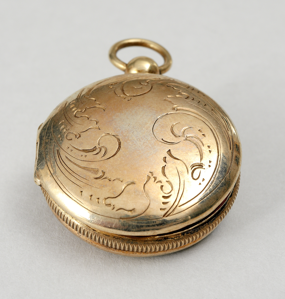 Medaljong av förgyllt silver. Utformad som en urboett. Runt kanterna stavdekor. Ytterboetterna varav den ena öppningsbar, är utvändigt graverade med med bladornament. Invändigt har den ett genombrutet inre boettlock försett med gångjärn. Gravyr i form av bladslingor. Medaljongen har förmodligen haft en s.k. luktsvamp placerad inuti. Medaljongen är helt förgylld in- och utvändigt. Stadstämpel F (möjligen Falkenberg). Mästarstämpel A.M, årtalsstämpel L5 (1865)
Inskrivet i huvudbok 1969.