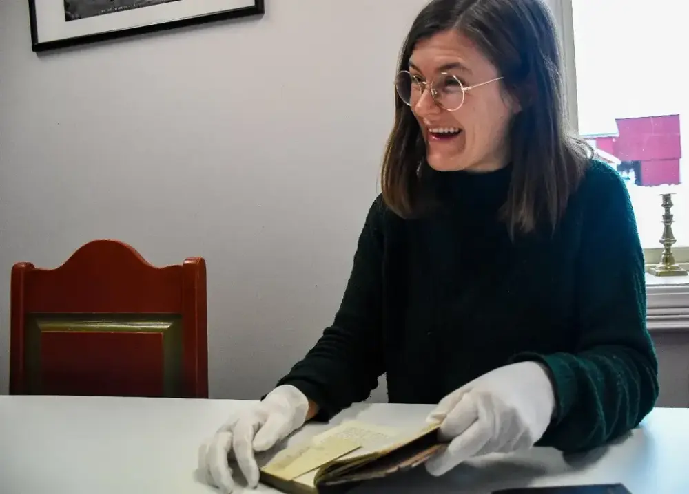 Smilende museumsansatt viser frem funnet av en barnetegning i en bok. 