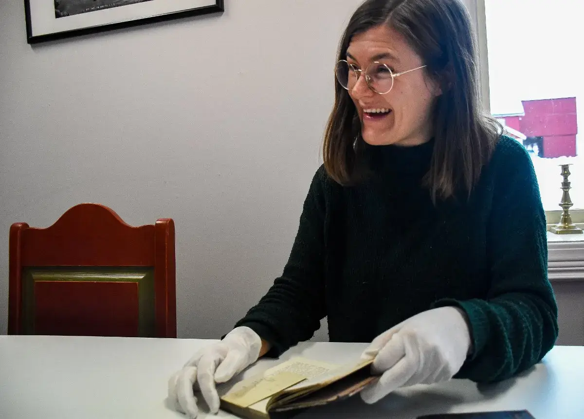 Smilende museumsansatt viser frem funnet av en barnetegning i en bok. 