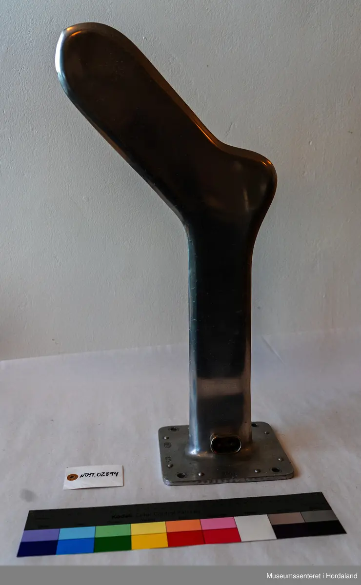 Sokkeform i metall. Den er flat og formet som en fot. Formen står opp fra en flat, rektangulær plate med hull i hvert hjørne.