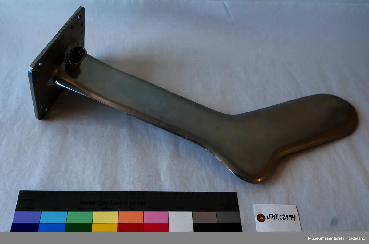 Sokkeform i metall. Den er flat og formet som en fot. Formen står opp fra en flat, rektangulær plate med hull i hvert hjørne.