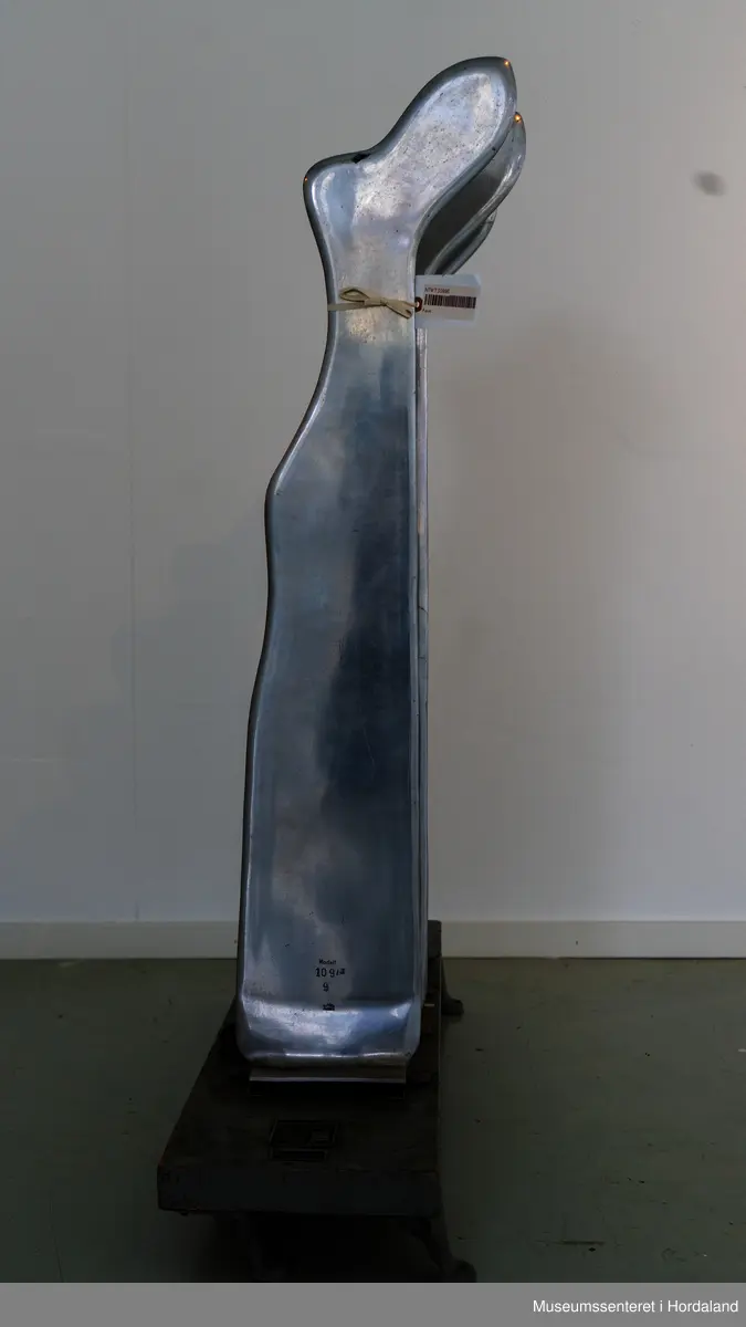 Fire strømpeformer i metall skrudd fast til rektangulær treplanke på fire metallføtter og to runde, svarte brytere av bakelitt. Strømpeformene er flate og formet som en fot. Treplate og metallføtter er gråmalte.