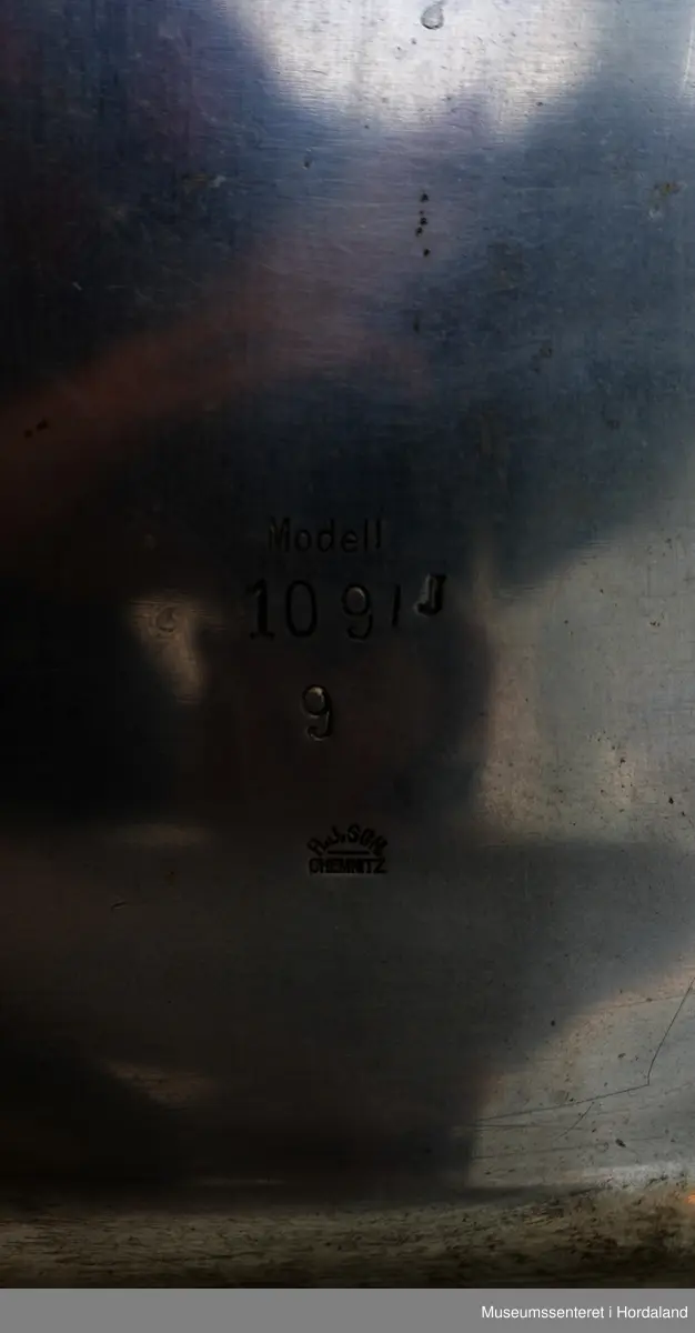 Fire strømpeformer i metall skrudd fast til rektangulær treplanke på fire metallføtter og to runde, svarte brytere av bakelitt. Strømpeformene er flate og formet som en fot. Treplate og metallføtter er gråmalte.