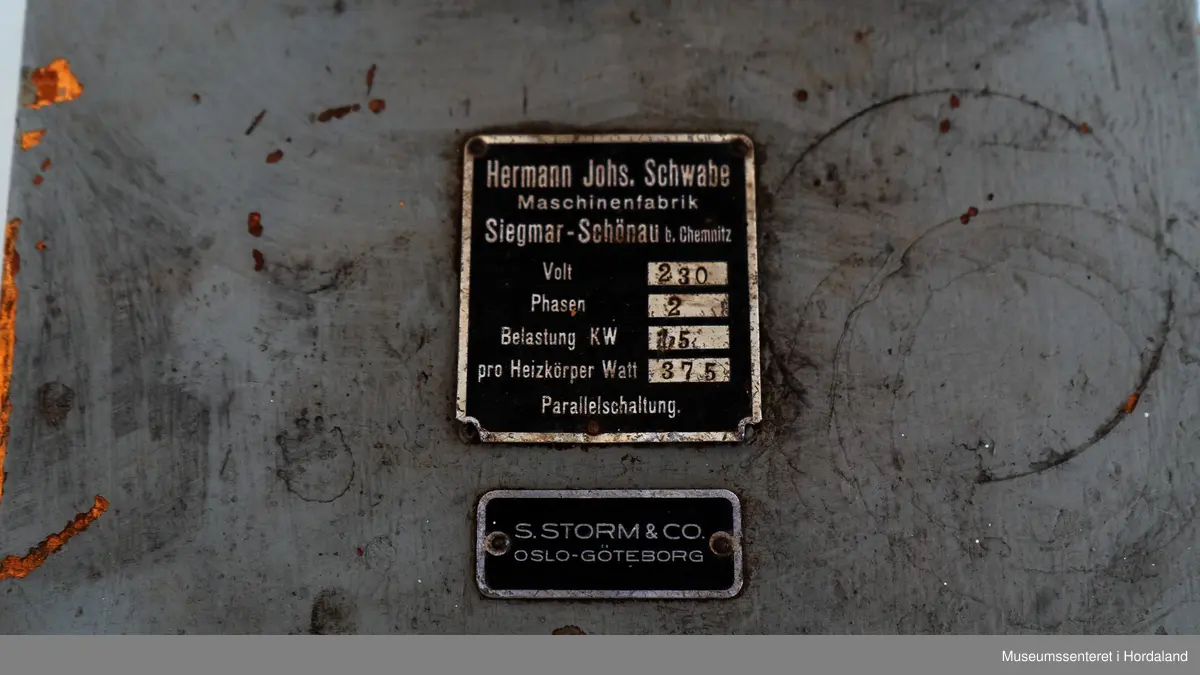 Fire strømpeformer i metall skrudd fast til rektangulær treplanke på fire metallføtter og to runde, svarte brytere av bakelitt. Strømpeformene er flate og formet som en fot. Treplate og metallføtter er gråmalte.