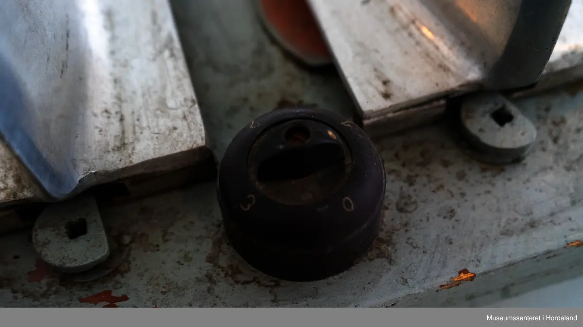 Fire strømpeformer i metall skrudd fast til rektangulær treplanke på fire metallføtter og to runde, svarte brytere av bakelitt. Strømpeformene er flate og formet som en fot. Treplate og metallføtter er gråmalte.