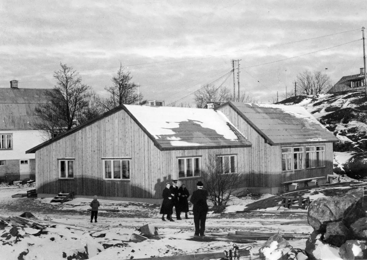 Den nybyggda skolan på Landsort. Den främre delen av byggnaden var lärarbostad och den bortre delen var skolsal. Skolan invigdes till Lucia 1958. 
Tre personer på väg sydvart: i mitten fyrmästaren Artur Öström, till höger om honom lärarinnan Karin Ollén. 