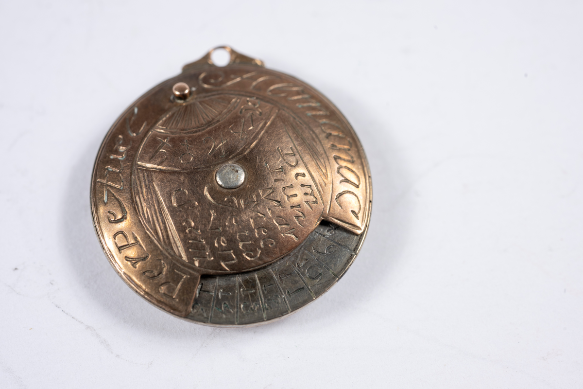 Vit och rödaktig metall, möjligen järn och koppar. Graverad på franska med månader, dagar, datum och zodiaksymboler. Gulddoublé kedja, länk och stav. 700 mm lång.