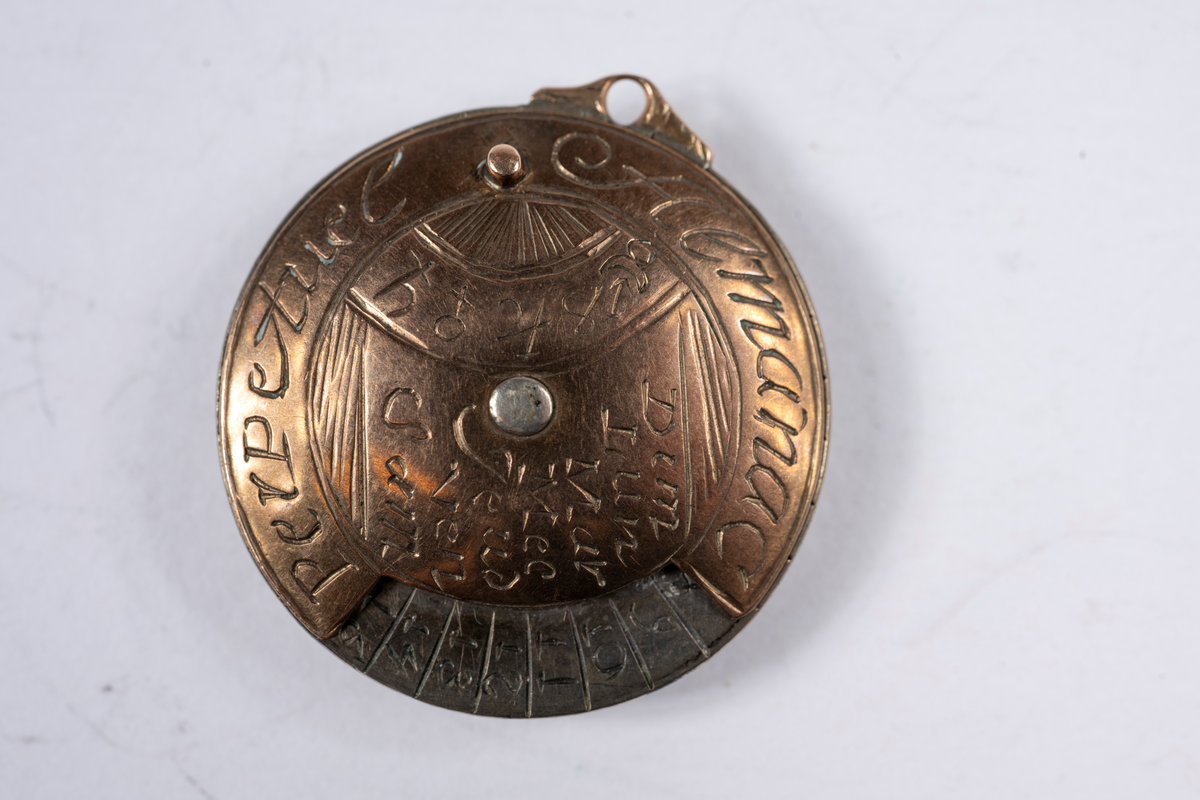 Vit och rödaktig metall, möjligen järn och koppar. Graverad på franska med månader, dagar, datum och zodiaksymboler. Gulddoublé kedja, länk och stav. 700 mm lång.