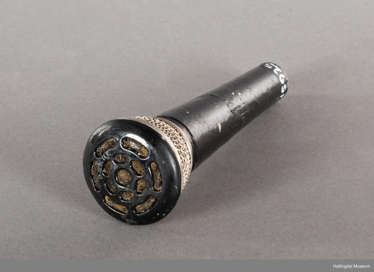 Mikrofon av merket Pearl. Svart kjegleformet håndtak med kabelkontakt i bunnen. Håndtaket kan se svartlakkert ut, mulig av bruker. Mikrofongrillen er av både metall og plast. 