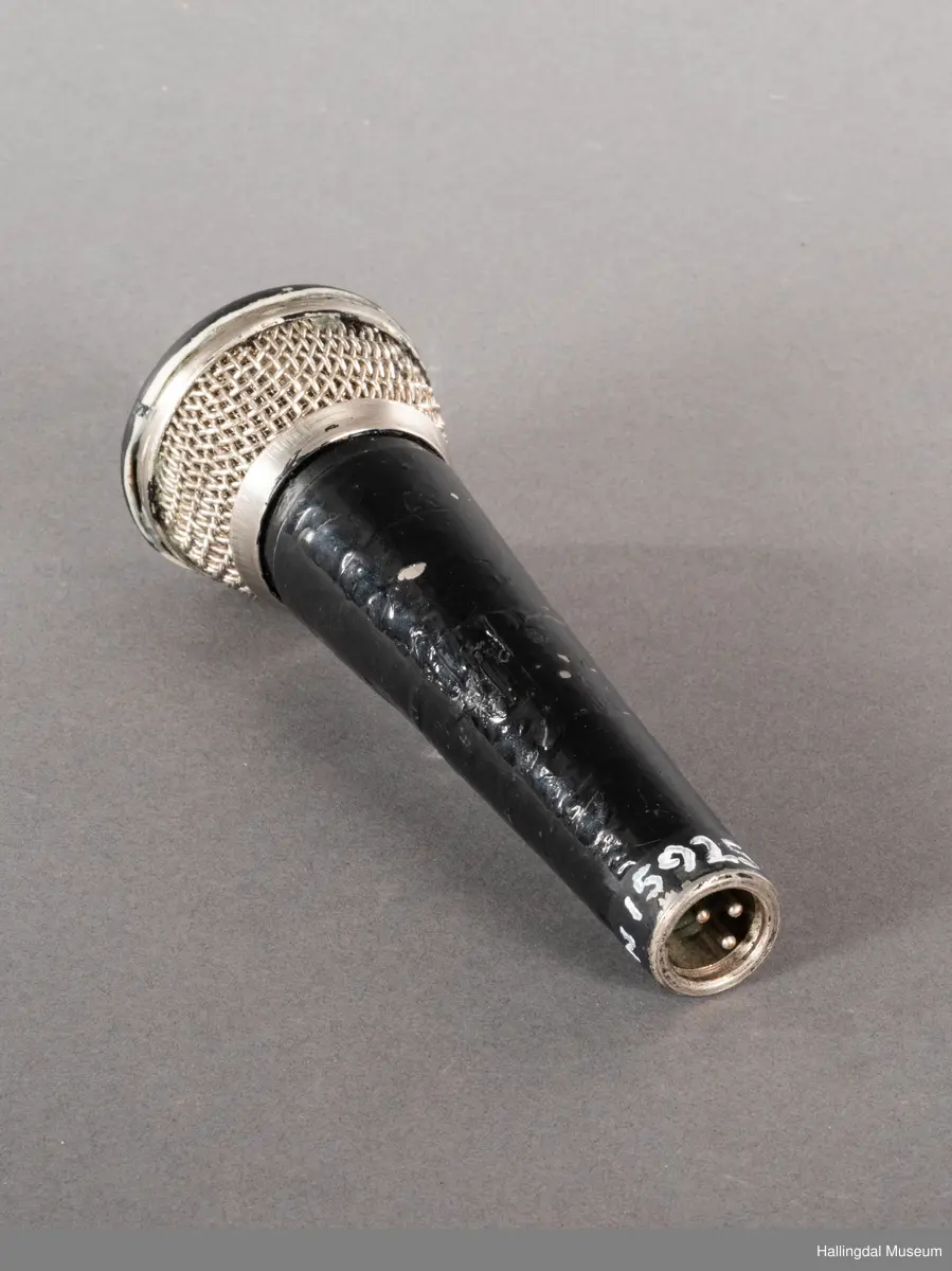 Mikrofon av merket Pearl. Svart kjegleformet håndtak med kabelkontakt i bunnen. Håndtaket kan se svartlakkert ut, mulig av bruker. Mikrofongrillen er av både metall og plast. 