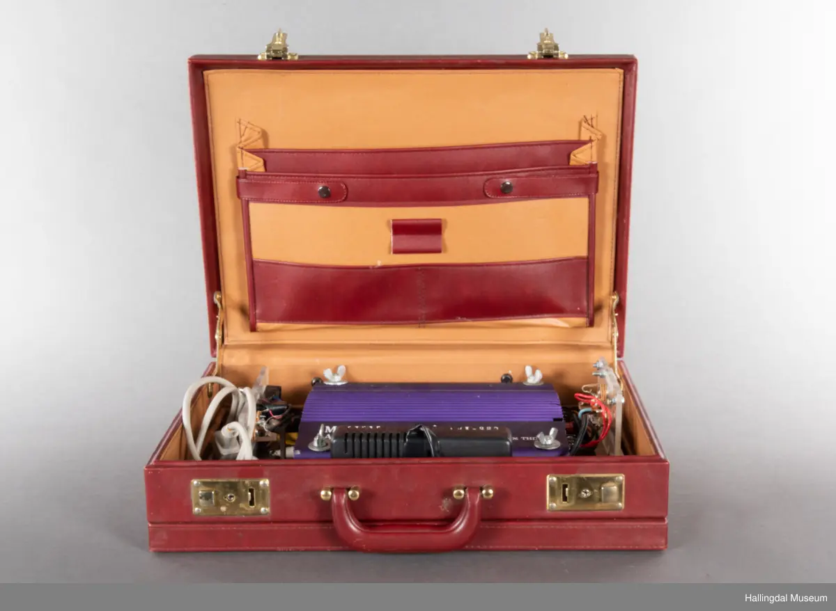 Hjemmelaget transportabelt lydanlegg. Rødbrun skinnkoffert med messingbeslag. Lysebrunt skinn innvendig fôr. Inneholder en ombygd "Mosfet" amplifier i lilla farge, med tilhørende grå strømkabel. På sidene er det plexiglass. Høyre side plexiglass bestående av strøminntak kontakt og en av og på bryter og to stk. merket mikserinngang til jack. På venstre side plexiglass inntak med merke: 12V - DG og to høytalerinnganger. Kabler til høytaler og mikrofon mangler.  
