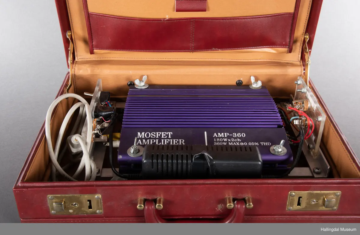 Hjemmelaget transportabelt lydanlegg. Rødbrun skinnkoffert med messingbeslag. Lysebrunt skinn innvendig fôr. Inneholder en ombygd "Mosfet" amplifier i lilla farge, med tilhørende grå strømkabel. På sidene er det plexiglass. Høyre side plexiglass bestående av strøminntak kontakt og en av og på bryter og to stk. merket mikserinngang til jack. På venstre side plexiglass inntak med merke: 12V - DG og to høytalerinnganger. Kabler til høytaler og mikrofon mangler.  