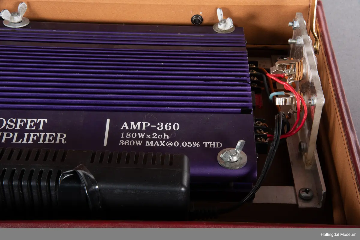 Hjemmelaget transportabelt lydanlegg. Rødbrun skinnkoffert med messingbeslag. Lysebrunt skinn innvendig fôr. Inneholder en ombygd "Mosfet" amplifier i lilla farge, med tilhørende grå strømkabel. På sidene er det plexiglass. Høyre side plexiglass bestående av strøminntak kontakt og en av og på bryter og to stk. merket mikserinngang til jack. På venstre side plexiglass inntak med merke: 12V - DG og to høytalerinnganger. Kabler til høytaler og mikrofon mangler.  