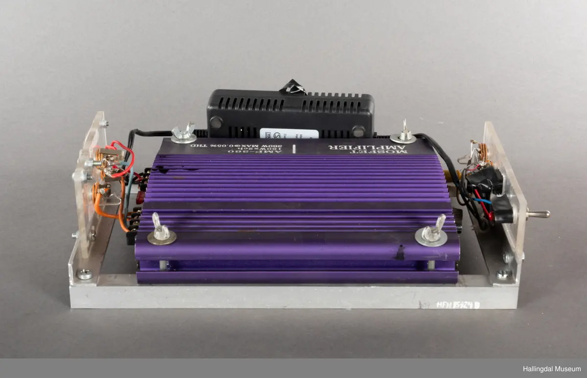 Hjemmelaget transportabelt lydanlegg. Rødbrun skinnkoffert med messingbeslag. Lysebrunt skinn innvendig fôr. Inneholder en ombygd "Mosfet" amplifier i lilla farge, med tilhørende grå strømkabel. På sidene er det plexiglass. Høyre side plexiglass bestående av strøminntak kontakt og en av og på bryter og to stk. merket mikserinngang til jack. På venstre side plexiglass inntak med merke: 12V - DG og to høytalerinnganger. Kabler til høytaler og mikrofon mangler.  