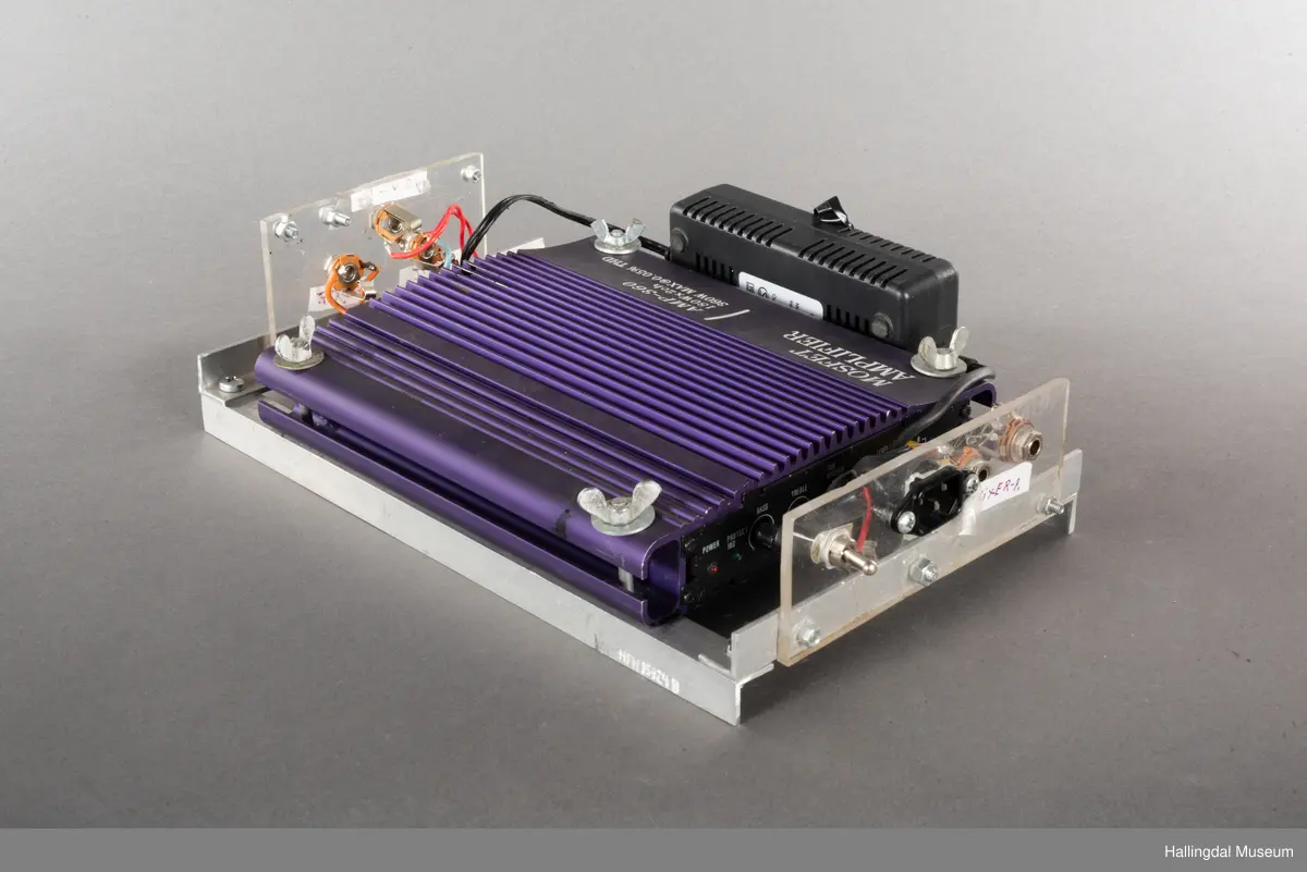 Hjemmelaget transportabelt lydanlegg. Rødbrun skinnkoffert med messingbeslag. Lysebrunt skinn innvendig fôr. Inneholder en ombygd "Mosfet" amplifier i lilla farge, med tilhørende grå strømkabel. På sidene er det plexiglass. Høyre side plexiglass bestående av strøminntak kontakt og en av og på bryter og to stk. merket mikserinngang til jack. På venstre side plexiglass inntak med merke: 12V - DG og to høytalerinnganger. Kabler til høytaler og mikrofon mangler.  