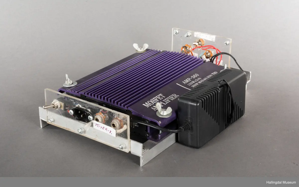 Hjemmelaget transportabelt lydanlegg. Rødbrun skinnkoffert med messingbeslag. Lysebrunt skinn innvendig fôr. Inneholder en ombygd "Mosfet" amplifier i lilla farge, med tilhørende grå strømkabel. På sidene er det plexiglass. Høyre side plexiglass bestående av strøminntak kontakt og en av og på bryter og to stk. merket mikserinngang til jack. På venstre side plexiglass inntak med merke: 12V - DG og to høytalerinnganger. Kabler til høytaler og mikrofon mangler.  