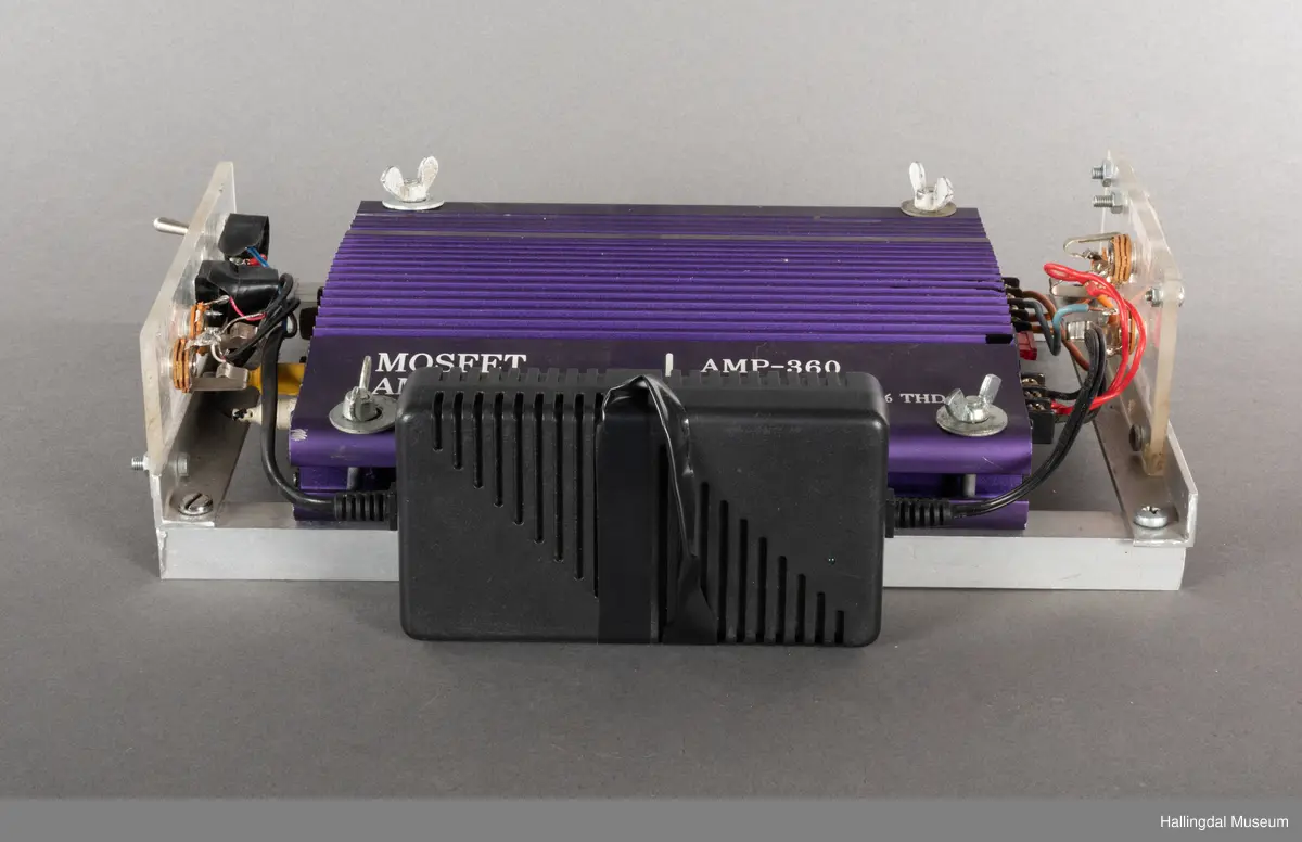Hjemmelaget transportabelt lydanlegg. Rødbrun skinnkoffert med messingbeslag. Lysebrunt skinn innvendig fôr. Inneholder en ombygd "Mosfet" amplifier i lilla farge, med tilhørende grå strømkabel. På sidene er det plexiglass. Høyre side plexiglass bestående av strøminntak kontakt og en av og på bryter og to stk. merket mikserinngang til jack. På venstre side plexiglass inntak med merke: 12V - DG og to høytalerinnganger. Kabler til høytaler og mikrofon mangler.  